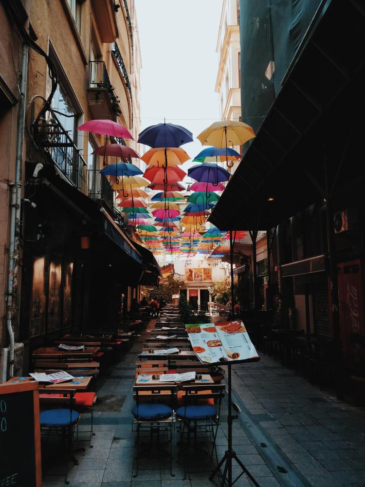 Many colorful umbrellas hanging above an alley over restaurant seating